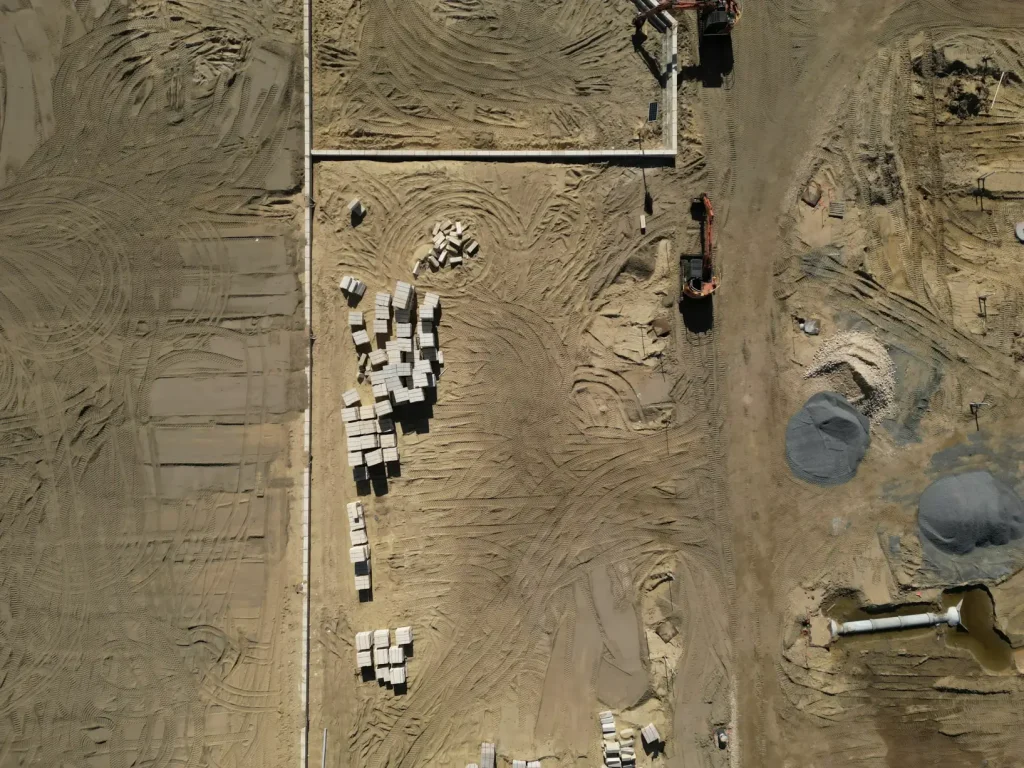 Aerial view of a levelled construction site with pallets of materials, foundations and plant set out on the sand