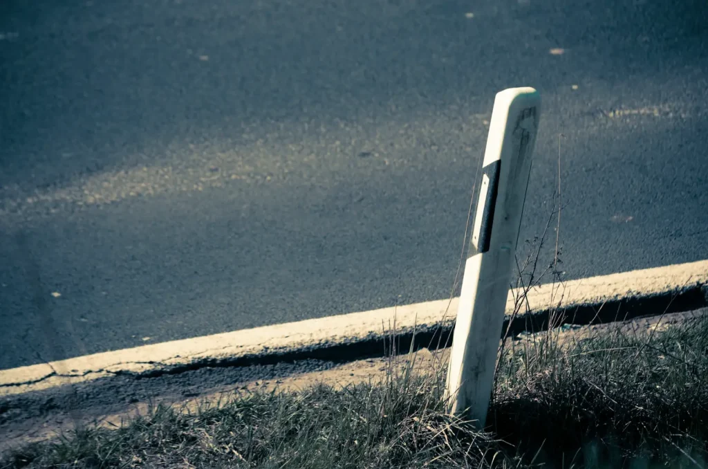 A white reflective marker post standing in the verge at the edge of a carriageway