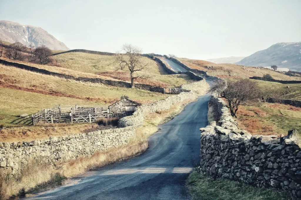 A narrow asphalt road winding between dry-stone walls through upland farmland